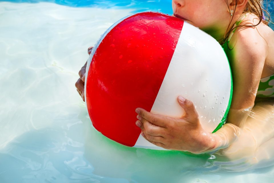 Little girl is playing with a ball in the pool into water on summer vacation in the courtyard