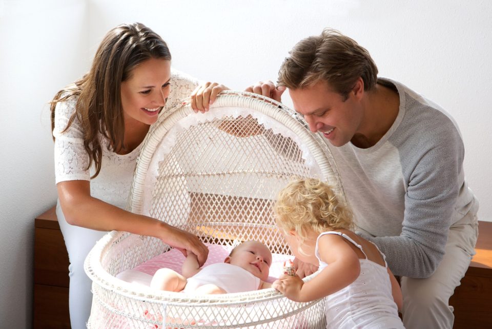 Young family smiling at newborn in cot