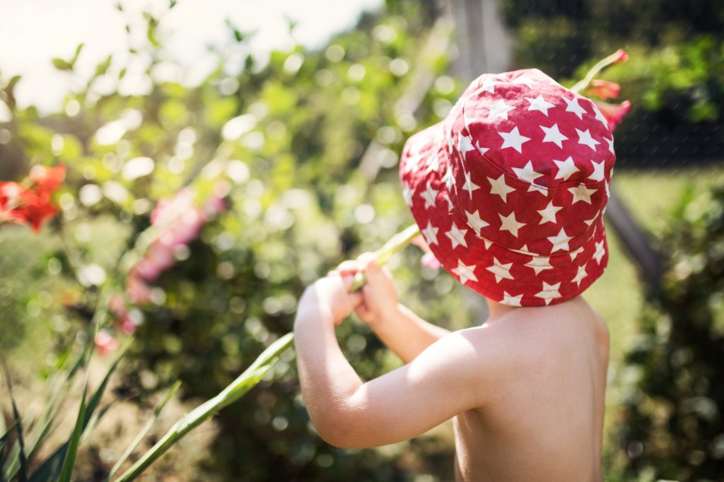 Rear view of small boy with a hat standing outdoors in garden in summer.