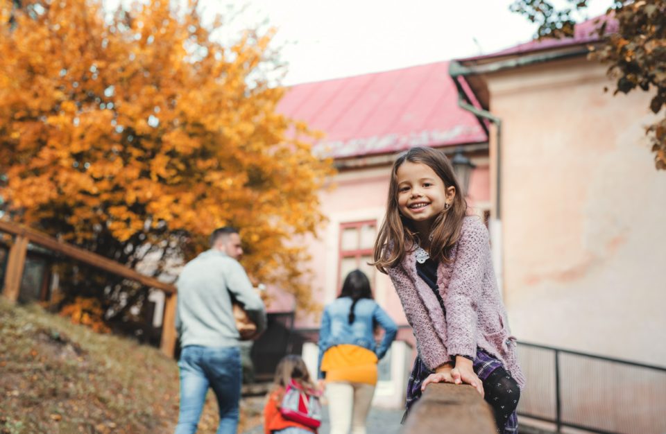 A portrait of small girl with her family in town in autumn.