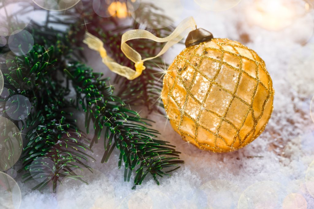 Golden Christmas ball on snow near branches of fir tree. Festive background with copy space