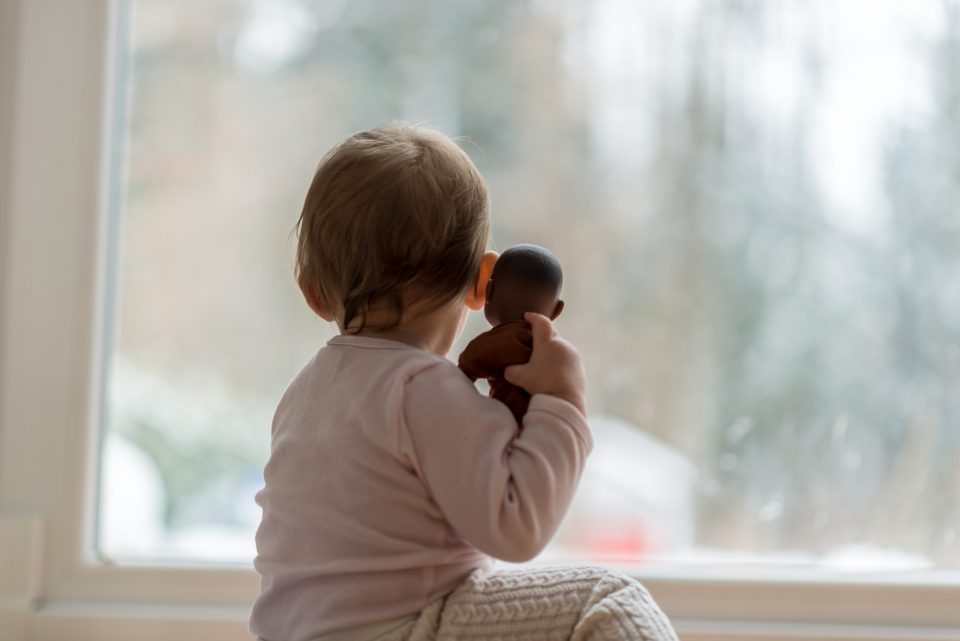 Little baby girl hugging a toy watching the winter snow outdoors