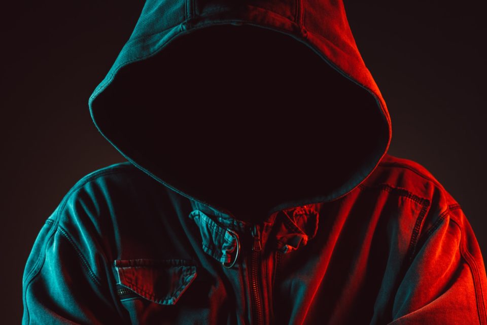 Red and blue lit low key portrait of hooded person