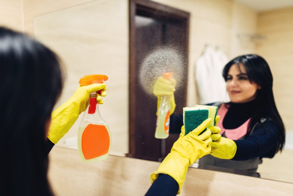 Housemaid cleans the mirror with a cleaning spray