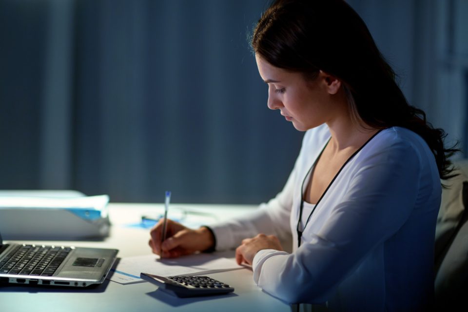 woman with calculator and papers at night office