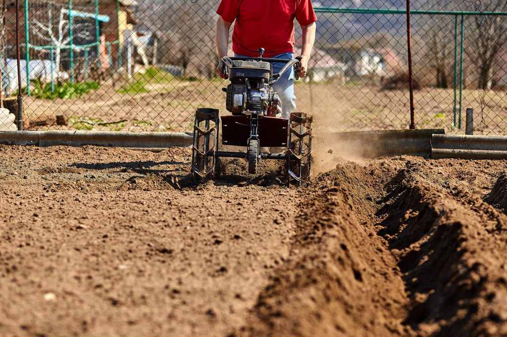 Gardener cultivate ground soil with tiller tractor or rototiller, cutivator