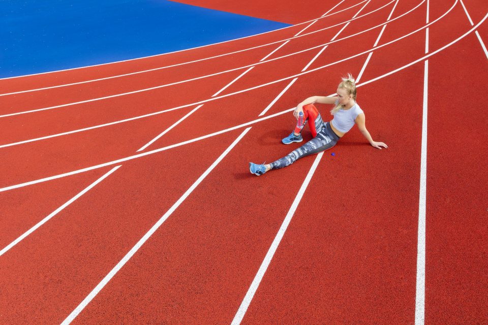 Athletic female runner rests on running track at sports arena