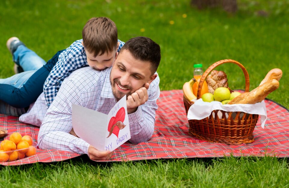 Best Father's Day greeting. Father and son with card cuddling on plaid in park during picnic