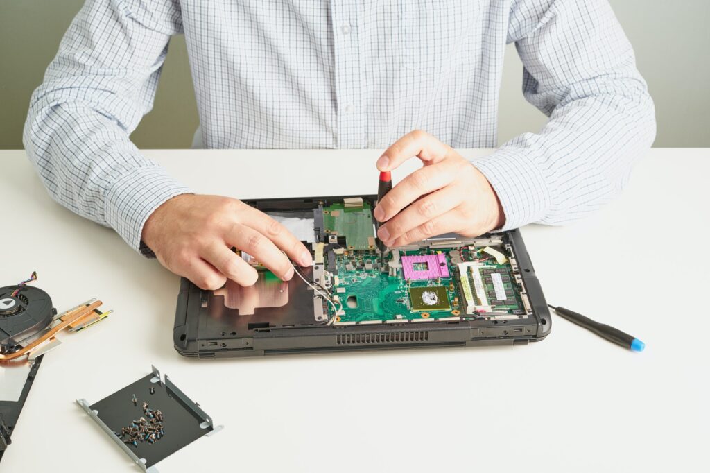 Man repairs computer. A service engineer in shirt repairs laptop, at white Desk against white wall.