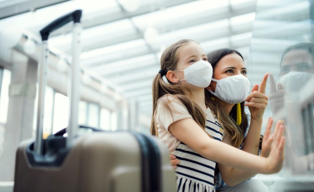 Mother with daughter going on holiday, wearing face masks at the airport