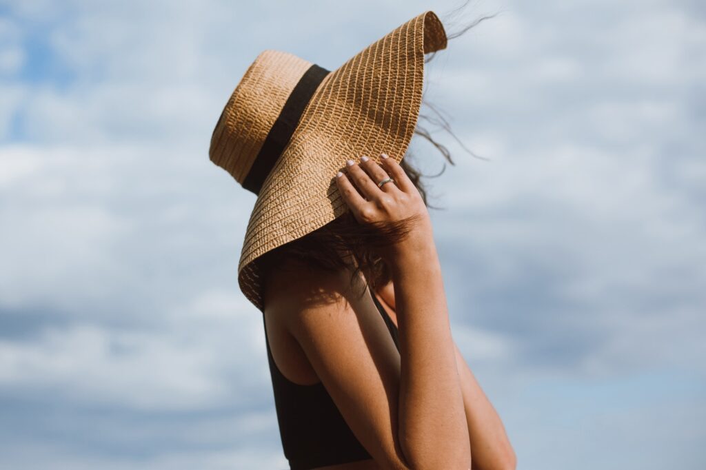 Tanned girl holding hat and posing on background of blue sky in hot summer day
