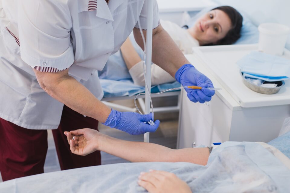 Nurse connecting an intravenous drip in hospital room.