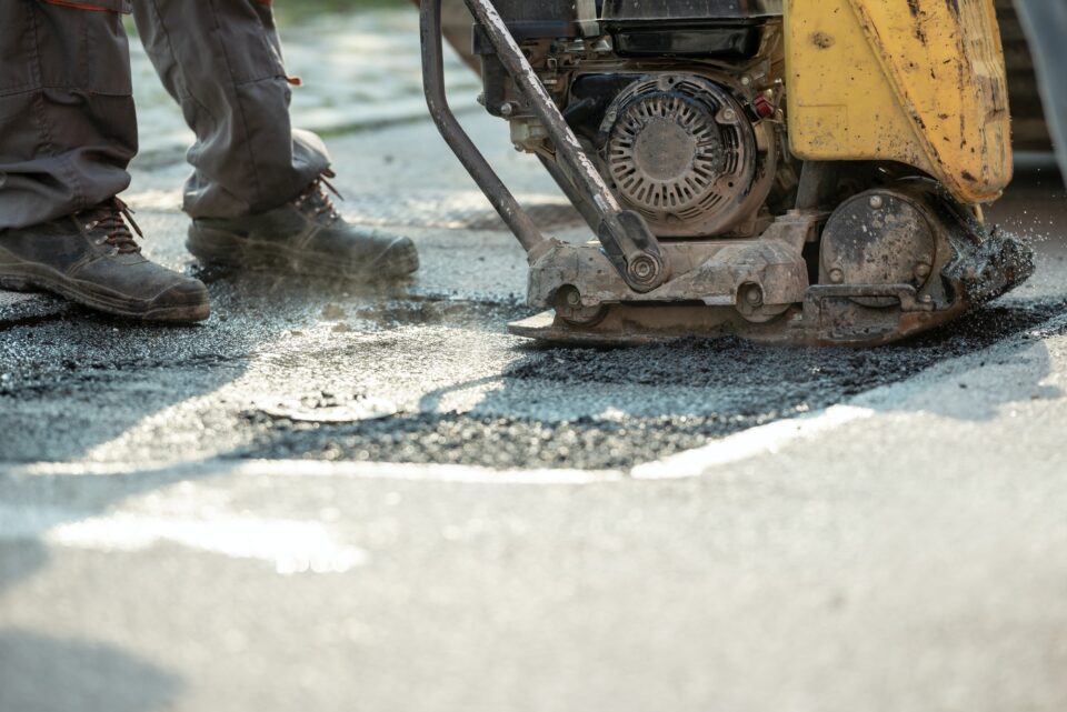 Worker using compactor to finish patching bump in the road