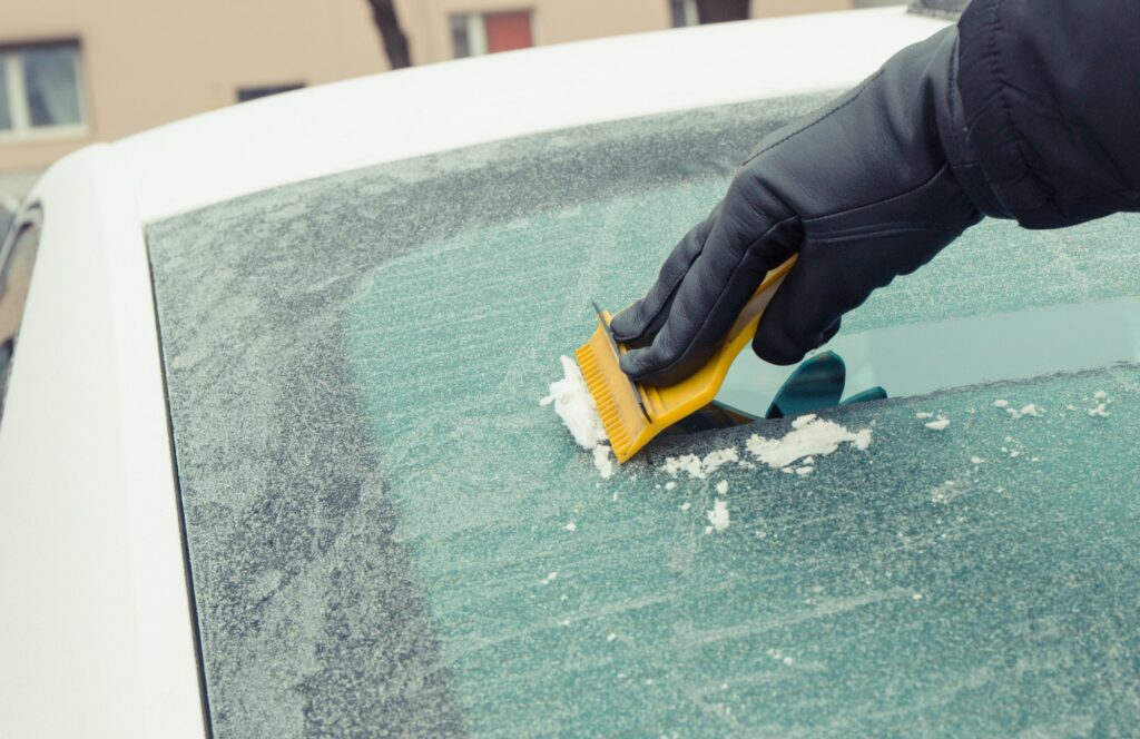 Hand holding yellow scraper and removing ice or snow from car window