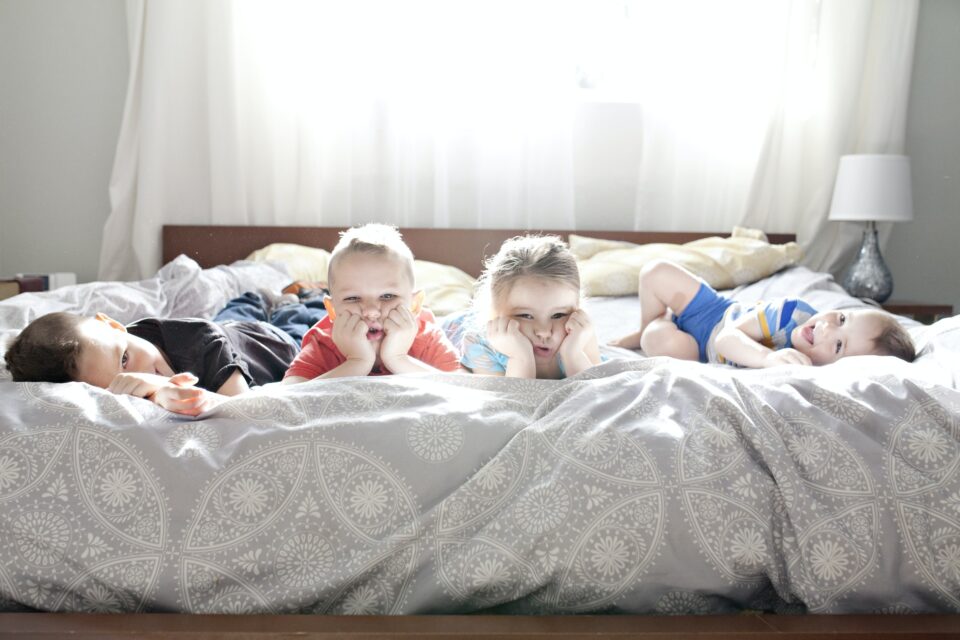 Four kids posing for a photo on a giant bed. They all look unhappy.