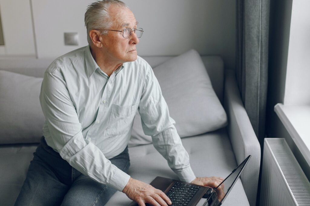 Elegant old man sitting at home and using a laptop