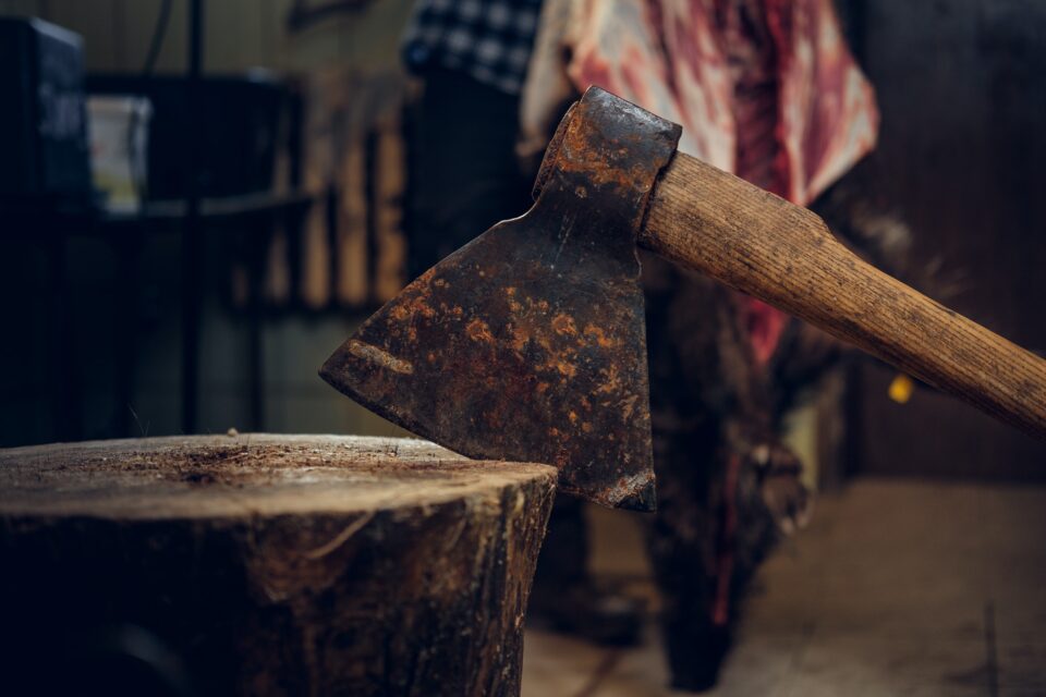 Close up image of axe over bearded butcher on background.