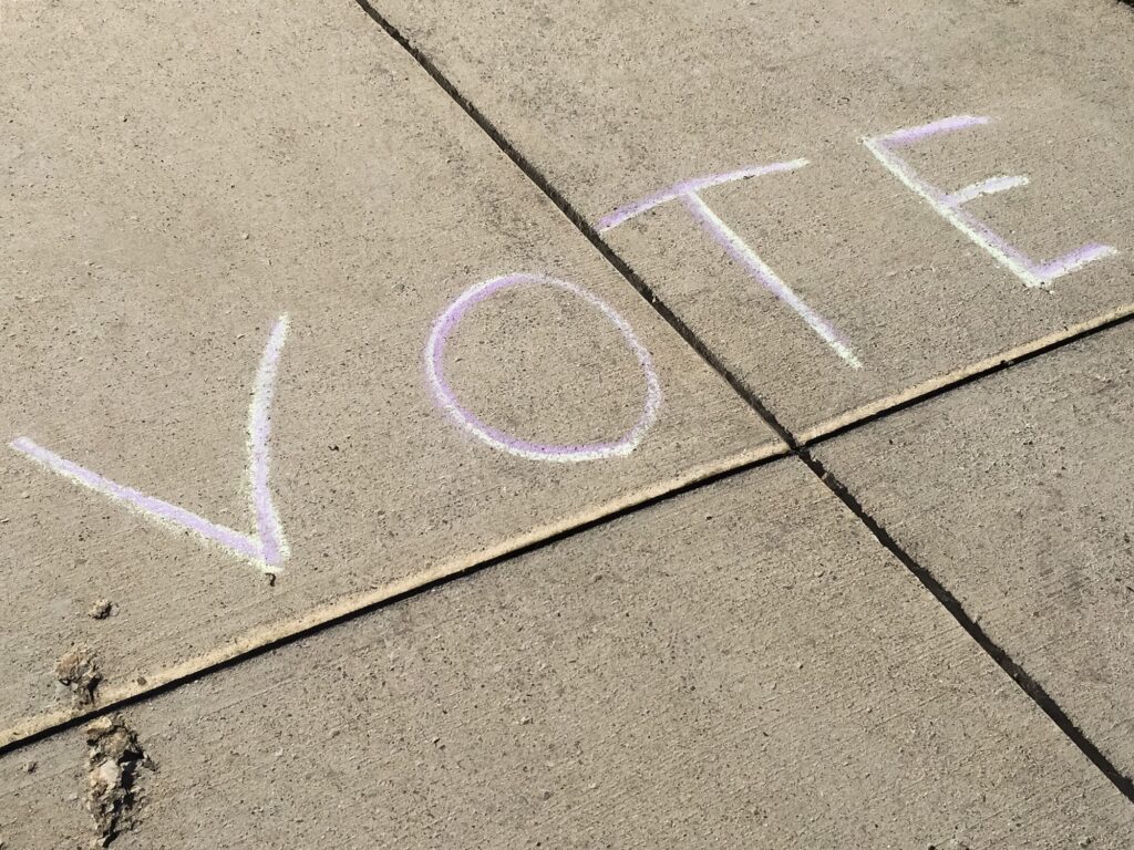 The word VOTE written with sidewalk chalk on pavement to remind people to go vote