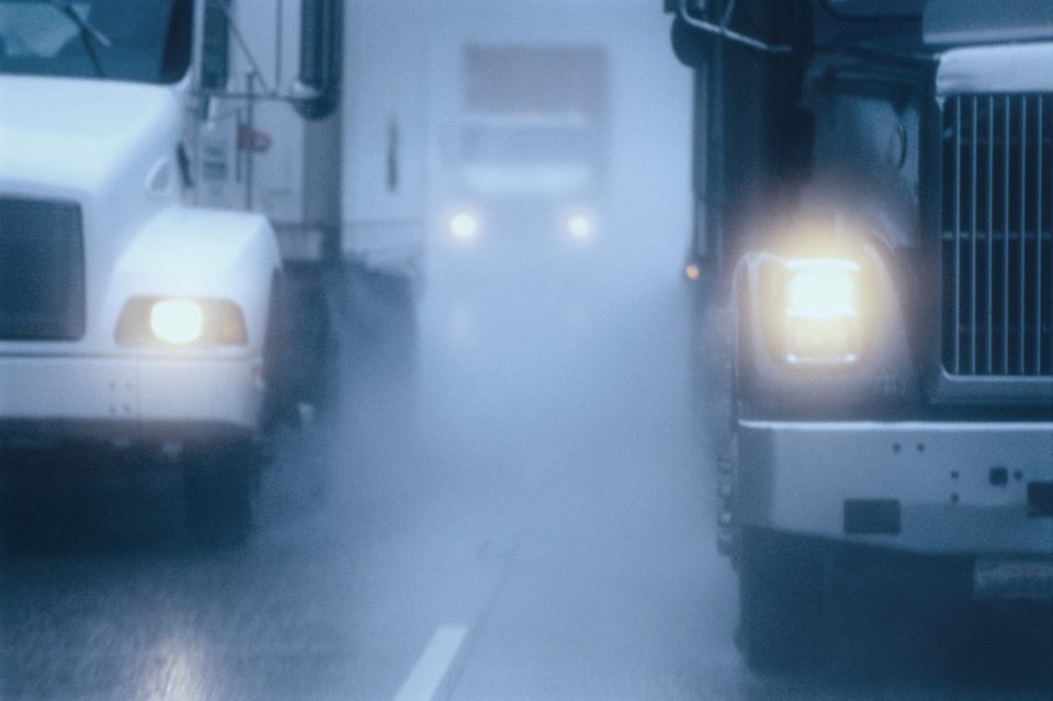 Partial view of large commercial truck driving in hazardous conditions of snow and rain on a