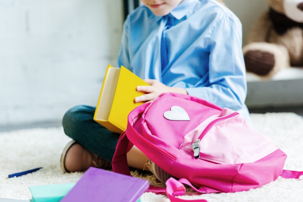 cropped shot of smiling child holding book while packing school bag