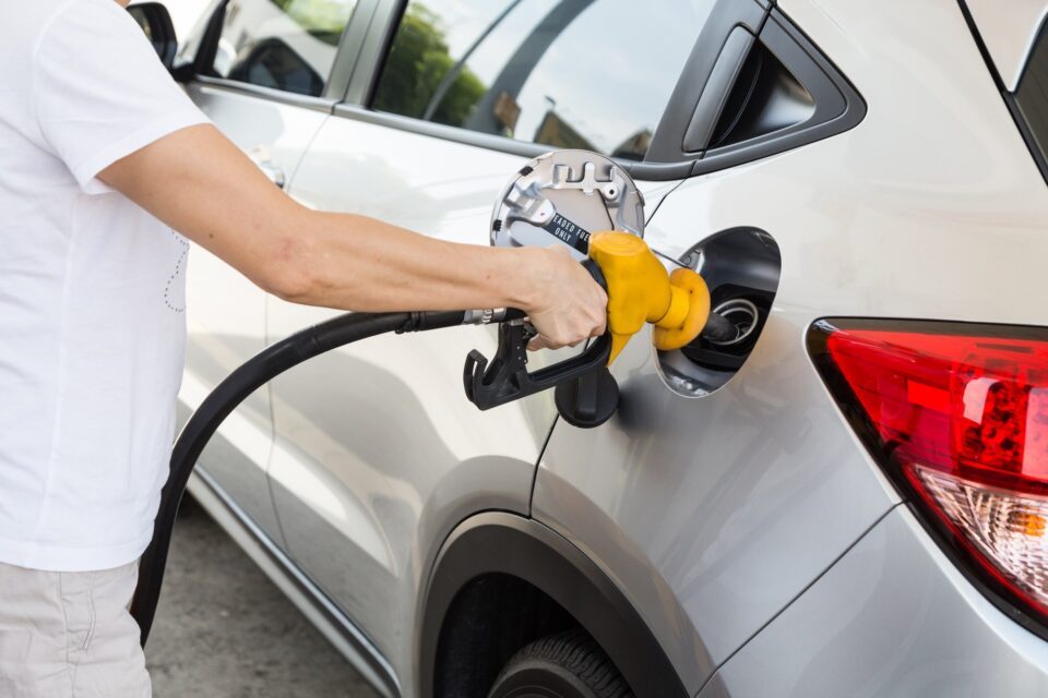 Person holding yellow nozzle filling petrol into car