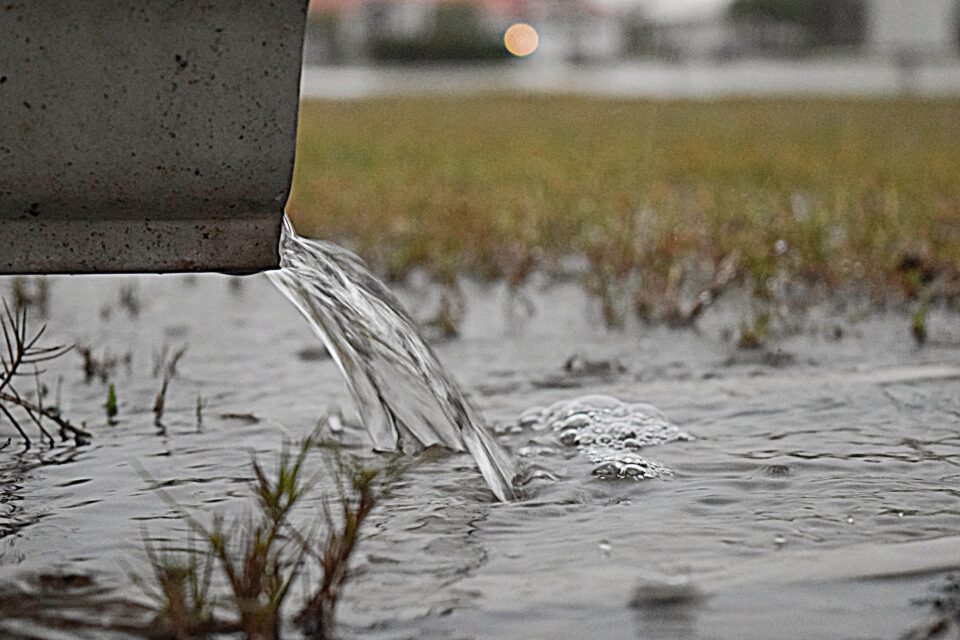 Rain pouring down a downspout to quench the drought-ravaged grass below