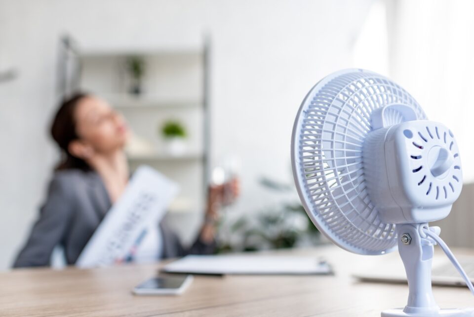 selective focus of businesswoman suffering from heat while sitting near electric fan