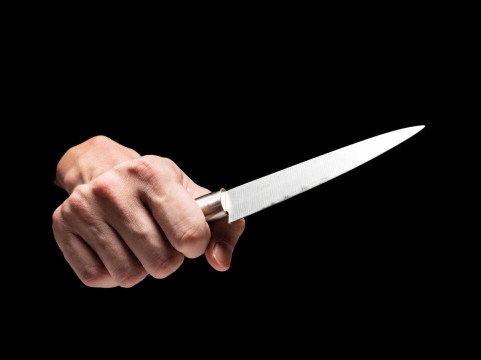 Male hand holding knife on black background.