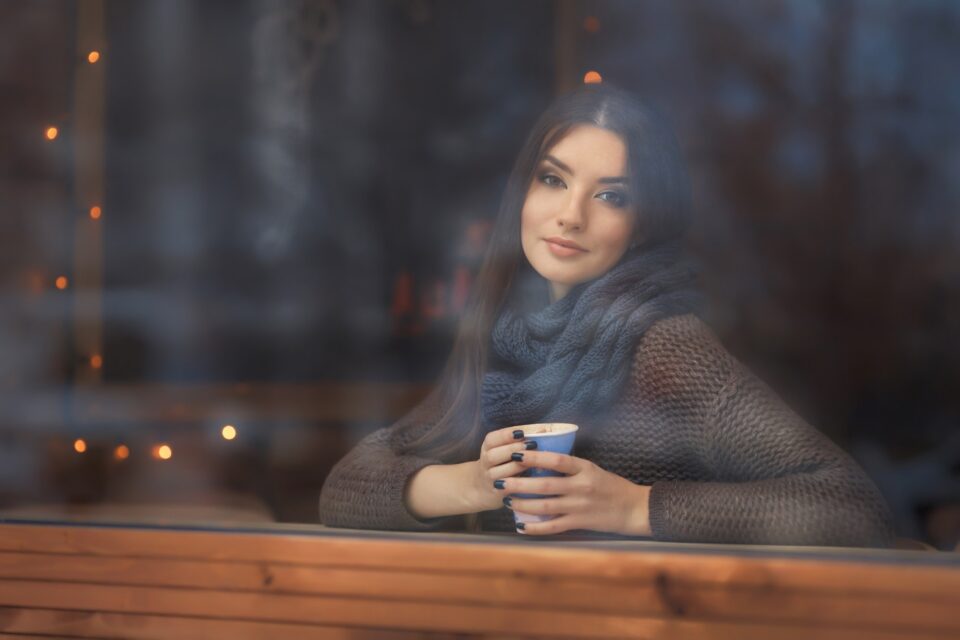 Portrait of beautiful young woman holding hot drink: a cup of tea in urban cafe