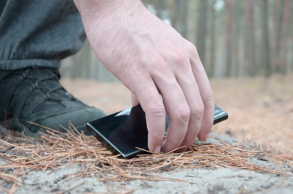 Male hand picking up lost mobile phone from a ground in autumn f